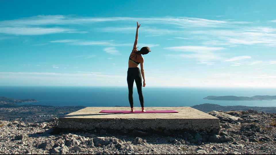 Girl in yoga clothes on hilltop overlooking the sea